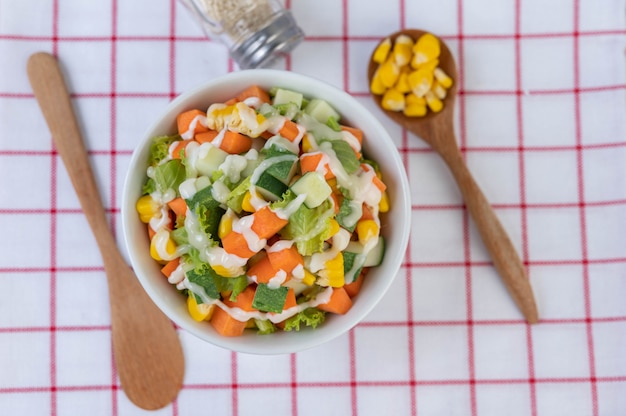 Salade de concombre, maïs, carotte et laitue dans une tasse blanche.