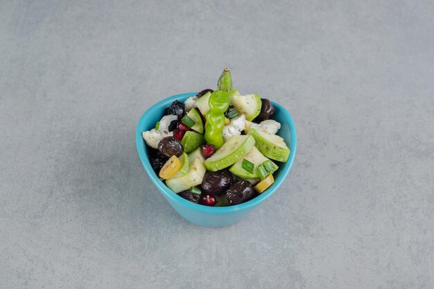 Salade dans une tasse bleue avec un mélange de légumes et de fruits hachés.