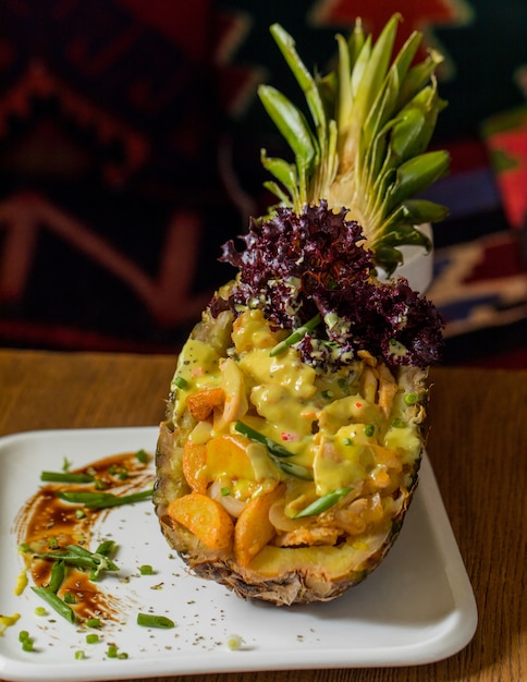 Salade de fruits mélangée servie à l'intérieur d'une ananas sculptée avec des herbes.