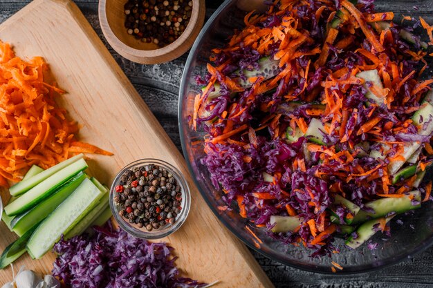 Salade de légumes dans un bol avec d'autres légumes hachés sur une planche à découper en gros plan sur un fond en bois foncé