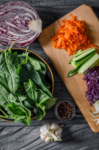 Une salade de légumes avec des légumes en tranches, des verts sur fond de bois foncé, vue de dessus.