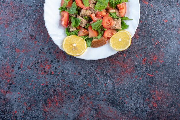 Salade de légumes mélangés avec garniture de citron et croûte séchée sur table noire.