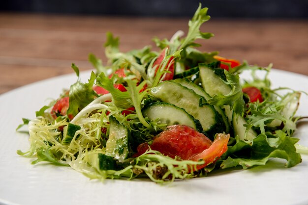 Salade de légumes en plaque ronde blanche sur table en bois.