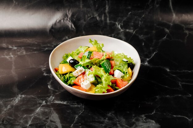 Salade de légumes de saison avec des aliments mélangés dans un bol blanc sur un marbre noir.