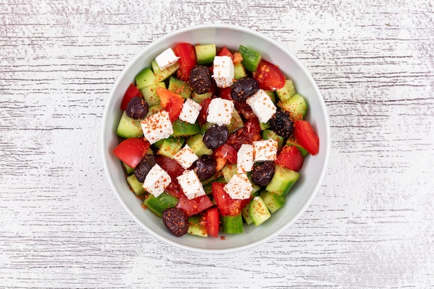 Salade de légumes tomate concombre olive dans un bol blanc sur la surface en bois vue de dessus des aliments sains