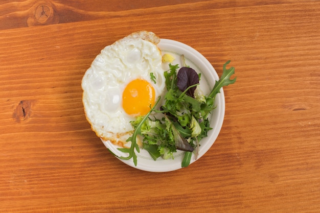 Salade et moitié oeuf au plat sur une assiette au-dessus de la table en bois