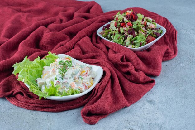 Salade d'Olivier avec laitue et salade de légumes mélangés dans des bols sur nappe sur surface en marbre