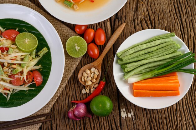 Salade de papaye (Som tum Thai) sur une plaque blanche sur une table en bois.