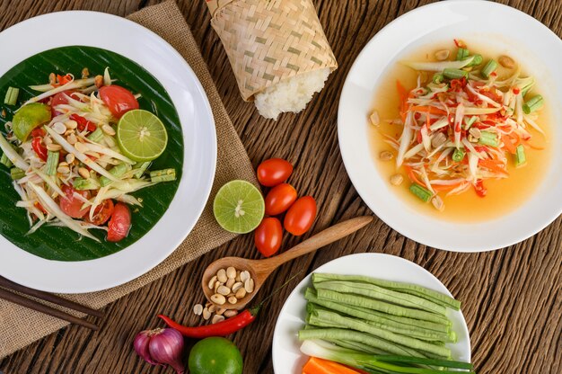 Salade de papaye (Som tum Thai) sur une plaque blanche sur une table en bois.