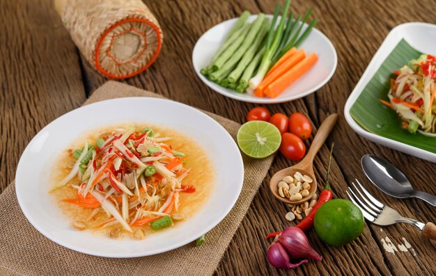 Salade de papaye (Som tum Thai) sur une plaque blanche sur une table en bois.