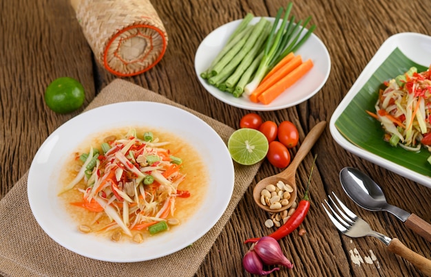 Salade de papaye (Som tum Thai) sur une plaque blanche sur une table en bois.