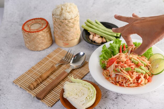 Salade de papaye thaïlandaise dans une assiette blanche avec du riz gluant