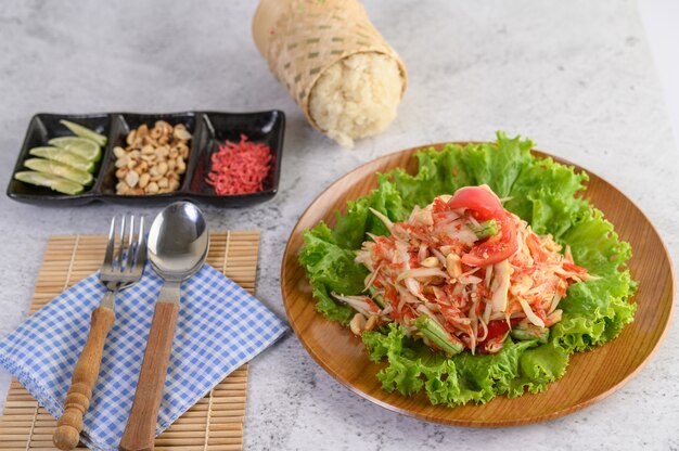 Salade de papaye thaïlandaise dans une assiette en bois avec du riz gluant et d'autres ingrédients