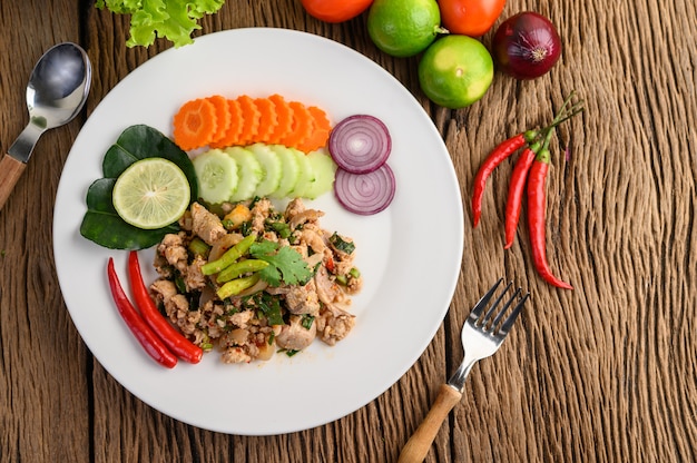 Photo gratuite salade de porc hachée épicée sur une plaque blanche sur une table en bois.