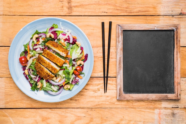 Salade de poulet Thai; baguettes et ardoise vierge sur table en bois