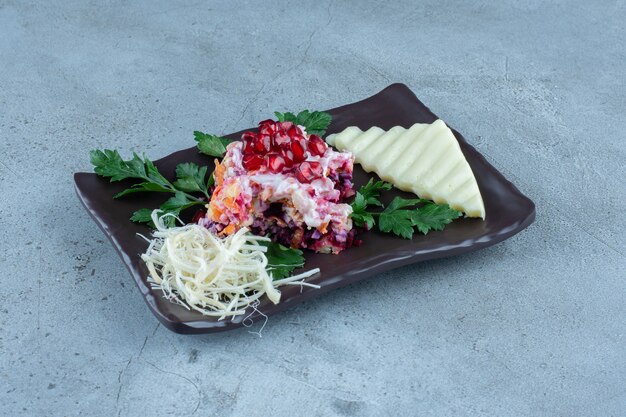 Salade servie avec du fromage tranché et râpé sur un plateau noir sur marbre.