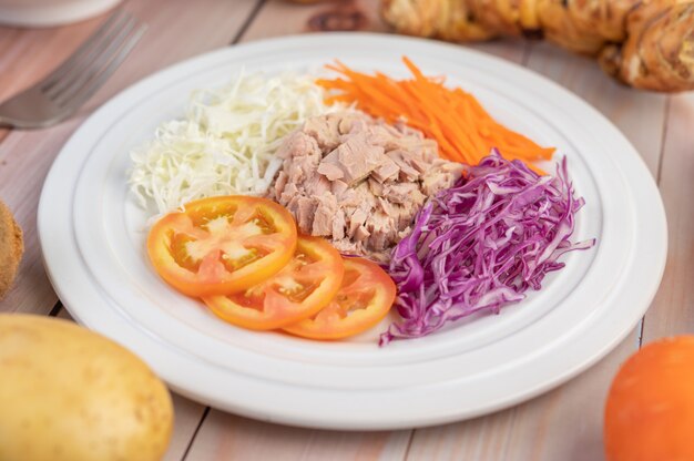 Salade de thon aux carottes, tomates, chou sur une plaque blanche sur un plancher en bois.