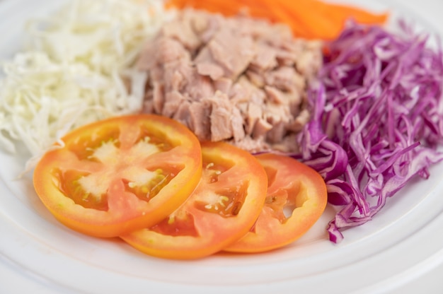 Salade de thon aux carottes, tomates, chou sur une plaque blanche sur un plancher en bois.