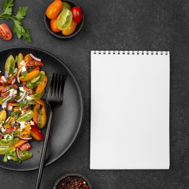 Salade de tomates vue de dessus avec fromage feta, roquette et cahier vierge