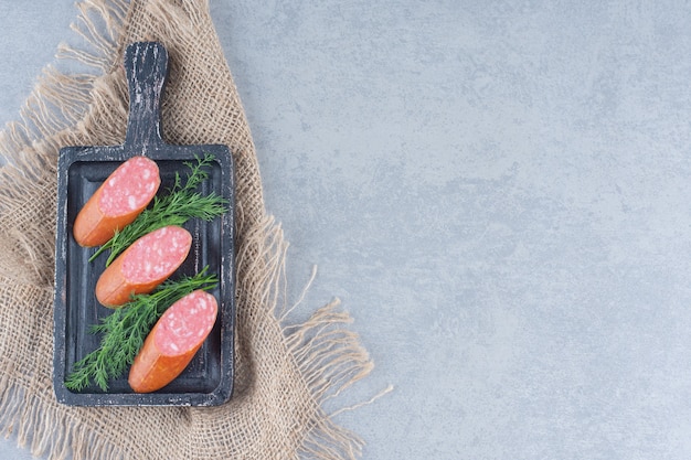 Photo gratuite salami frais avec des feuilles de fenouil sur une planche à découper noire.