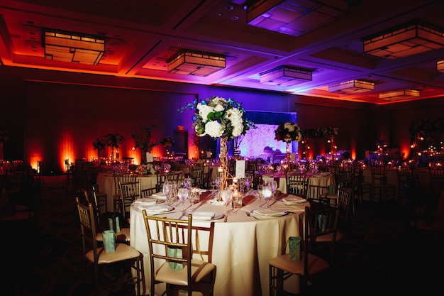Salle de banquet décorée avec table ronde servie avec centre d'hortensia et chaises chiavari