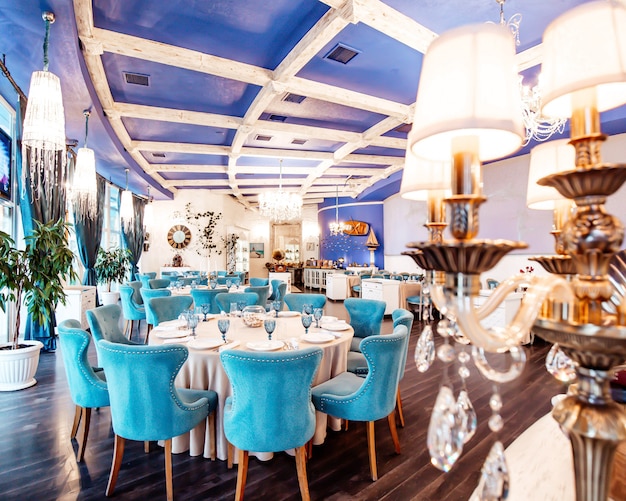 Salle de restaurant avec chaises turquoise, plafond de couleur marine, lustres classiques et murs blancs