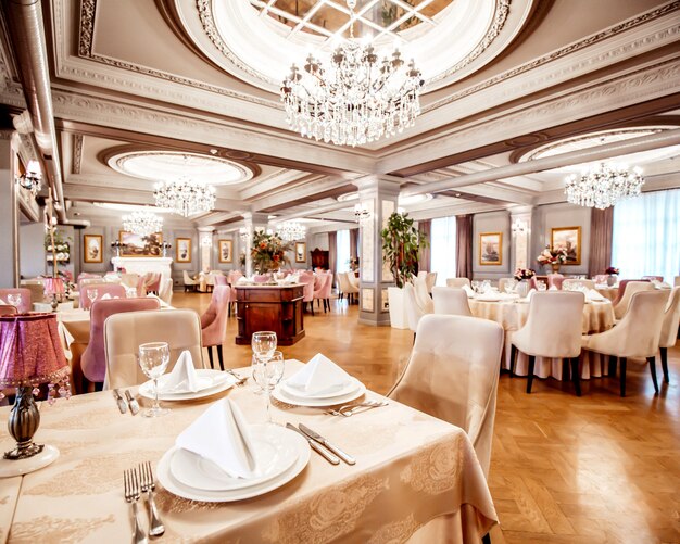 Salle de restaurant avec tables rondes et carrées quelques chaises et plantes