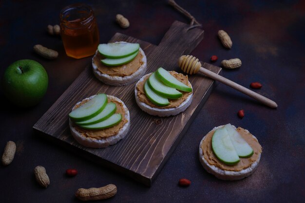 Sandwich au beurre de cacahuète naturel croquant avec du pain de gâteau de riz et des tranches de pomme verte et du miel.