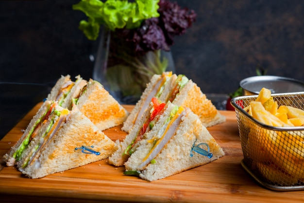 Sandwich club vue latérale avec frites dans une planche de service en bois