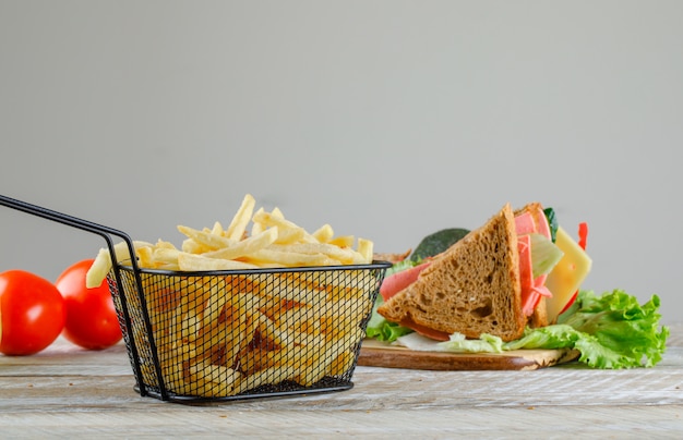 Sandwich avec frites, tomates vue latérale sur table en bois et gris