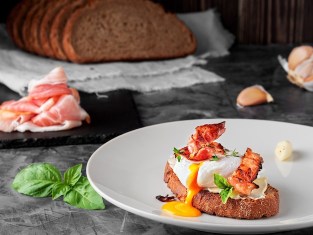 Sandwich à l'oeuf poché, jambon frit et fromage à la crème, garni de feuilles de basilic