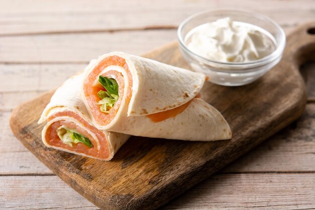 Sandwich roulé au saumon avec fromage et légumes sur table en bois