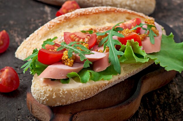 Sandwich avec saucisse, laitue, tomate et roquette sur l'ancienne surface en bois