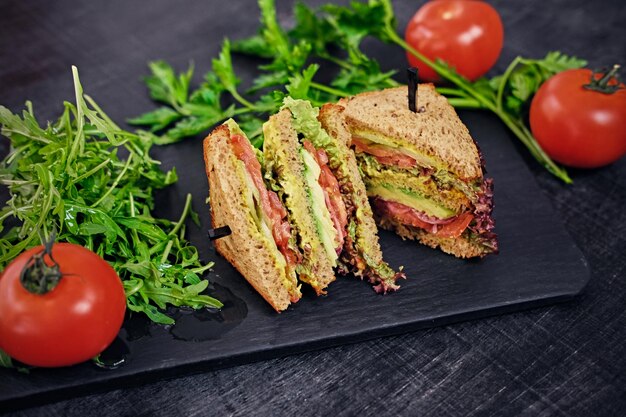 Sandwich végétarien avec salade et tomates sur une surface de table en bois.