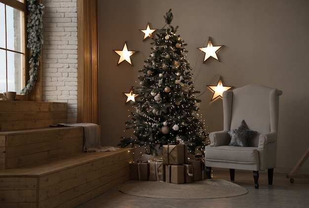 Sapin de noël décoré avec des cadeaux et fauteuil gris avec des étoiles suspendues