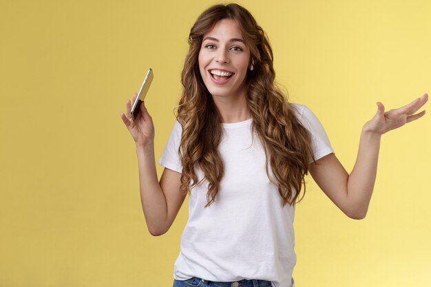 Sassy gai insouciant attrayant fille moderne coiffure frisée s'amusant humeur vive animée rythme du corps en mouvement serrer la main tenir la synchronisation des lèvres du smartphone porter des écouteurs sans fil écouter de la musique danser