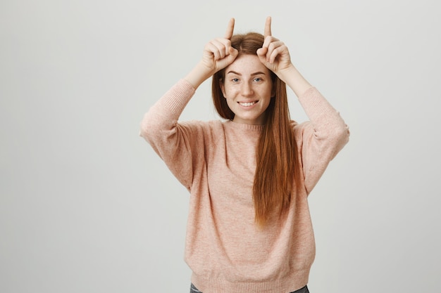 Sassy jolie fille rousse montrant des cornes de diable sur la tête