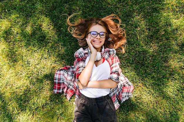 Satisfait jeune femme exprimant le bonheur dans le parc. Portrait de frais généraux de jolie fille couchée sur l'herbe verte.