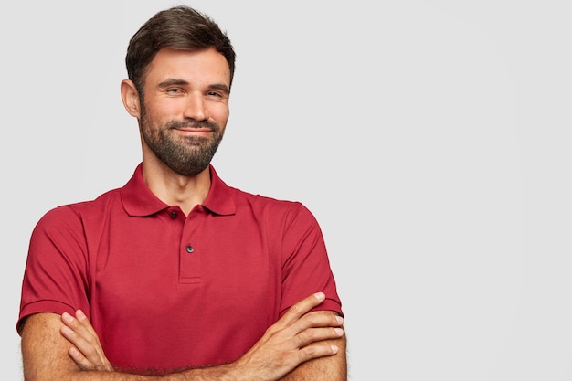 Satisfait jeune homme émotionnel posant contre le mur blanc