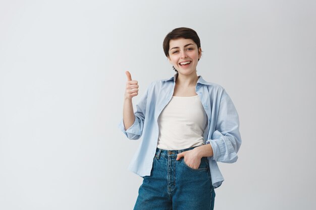 Satisfaite, belle femme aux cheveux courts montrant le pouce en l'air en signe d'approbation, louange un excellent choix