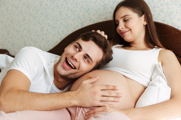 Satisfaite jeune femme enceinte couchée dans son lit avec son mari