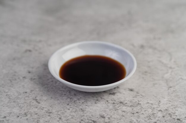 La sauce noire dans une petite tasse blanche posée sur le sol en ciment.