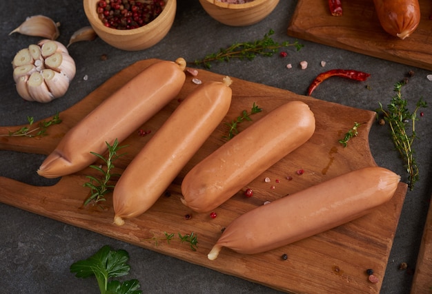 Photo gratuite saucisses crues fraîches et ingrédients pour la cuisine. saucisses de porc à la viande bouillie classique sur planche à découper avec poivre, romarin, herbes et épices.