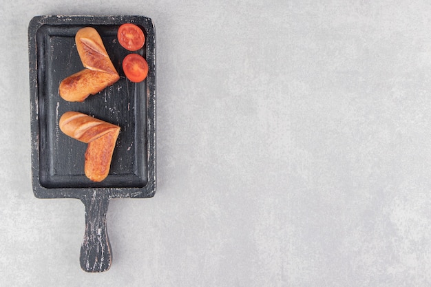 Saucisses frites aux tomates sur tableau noir.