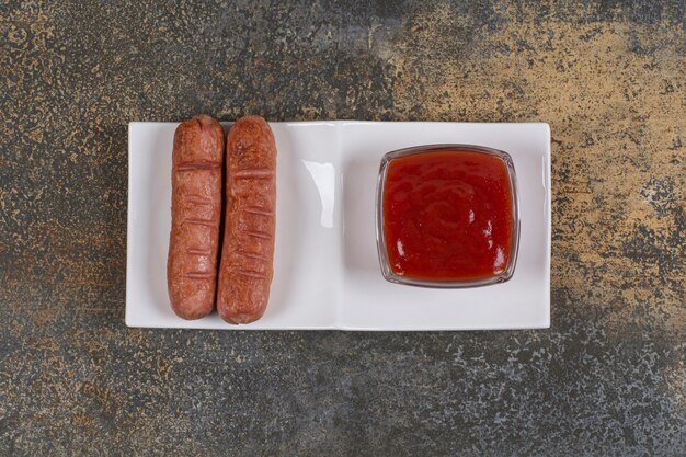 Saucisses frites et ketchup sur plaque blanche.