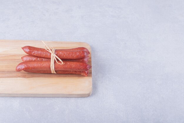 Saucisses fumées attachées avec une corde sur planche de bois.