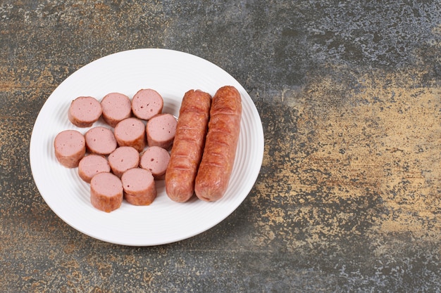 Saucisses grillées en tranches sur plaque blanche.