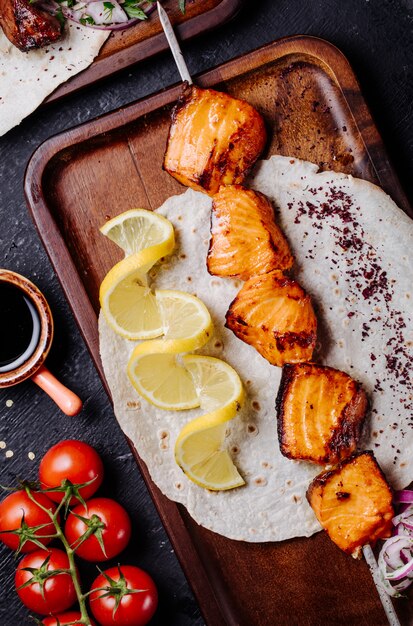 Saumon grillé servi dans du pain lavash avec des tranches de citron.