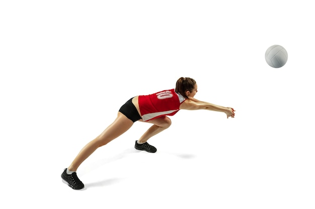 En saut et en vol. Jeune joueuse de volley-ball isolée sur fond de studio blanc. Femme en vêtements de sport et baskets s'entraînant, jouant. Concept de sport, mode de vie sain, mouvement et mouvement.