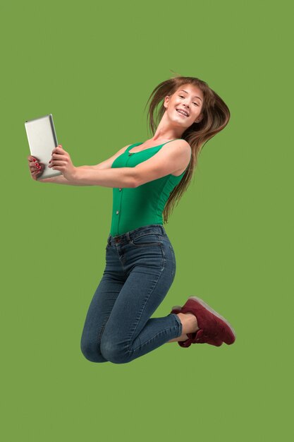 Sauter de jeune femme au vert à l'aide d'un gadget pour ordinateur portable ou tablette en sautant Fille en cours d'exécution en mouvement ou en mouvement